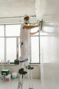 Construction worker smoothing a wall indoors using safety gear.